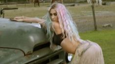 a woman with pink and blue hair leaning on the hood of an old pickup truck