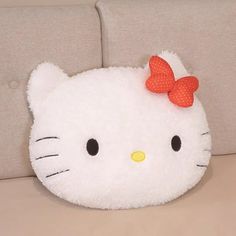 a white hello kitty pillow with a red bow on it's head sitting on a couch