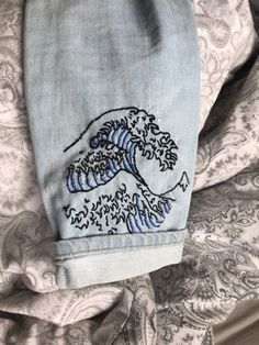 the back of a pair of jeans with an embroidered wave design on one side and blue stripes on the other