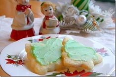 two cookies on a plate with green frosting and christmas decorations in the back ground