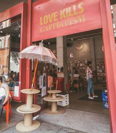 people sitting at tables in front of a red building with love kills capitalism written on it