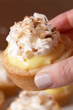 a hand holding a pastry with white frosting and toppings on it's top