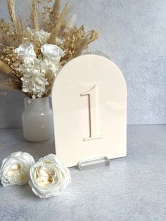 a white table number sitting next to a vase filled with flowers and dry grass on a gray surface