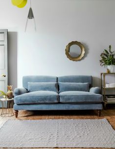 a blue couch sitting on top of a wooden floor next to a mirror and potted plant