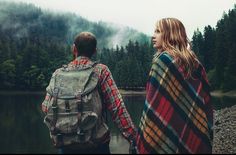 two people holding hands while standing next to a lake