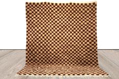 a brown and white checkered rug with fringes on the floor in front of a wall