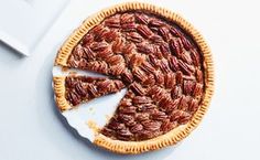 a pecan pie with one slice cut out and sitting on a white surface next to a knife