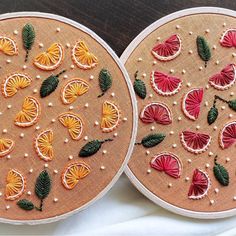 two hand embroidered oranges with leaves and flowers on them, sitting next to each other