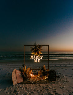 a sign that reads marry me on the beach at night with palm trees and candles