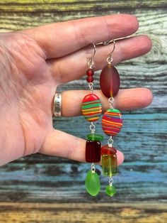 These are unique, fun and asymmetric, dangly, handmade earrings made from pressed, and recycled glass beads and rainbow calsilicate with stainless steel earwires. Stainless steel is hypoallergenic and will not produce skin irritation or discolouration. Stainless steel is corrosion and stain resistant. These earrings measure approximately 4 inches from the hook. Made by me in my Toronto studio, these earrings would be a great accessory for any occasion; casual, to work, and on to evening. Each item will come in its own organza bag, perfect for gifting! Please read store policies prior to purchase and feel free to contact me with any questions you may have.  Kindly ensure that you have provided a phone number in the personalization field as I am required to provide that for any parcel going Fun Green Beaded Earrings For Gift, Green Fun Beaded Earrings For Gift, Green Dangle Earrings With Recycled Glass, Vibrant Green Dangle Jewelry, Green Dangle Earrings In Recycled Glass, Green Recycled Glass Dangle Earrings, Vibrant Green Dangle Earrings, Recycled Glass Bead, Red Glass