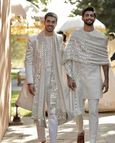 two men dressed in white outfits walking down the street with one wearing a shawl