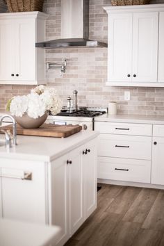 a kitchen with white cabinets and wood flooring is pictured in this image, there are flowers on the counter