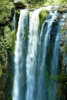 there is a large waterfall with water cascading down it's sides in the woods