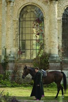 a man standing next to a brown horse in front of a building with arched windows