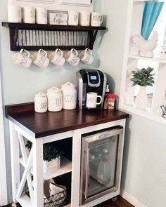 a coffee bar with cups and mugs on the shelf above it, in a kitchen