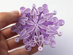 a hand holding a purple origami flower with buttons on it's petals