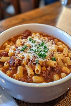 a white bowl filled with pasta and meat on top of a wooden table next to a fork