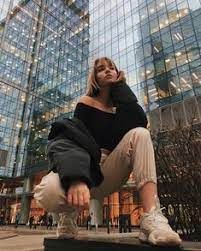 a woman sitting on top of a bench in front of tall glass buildings at night