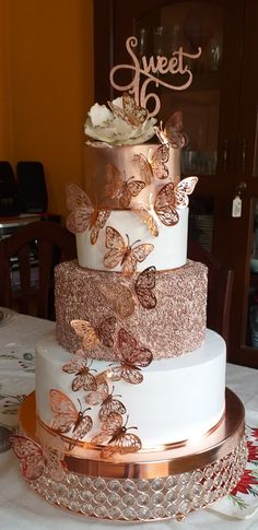 a three tiered wedding cake with gold butterflies on the top and bottom, sitting on a table