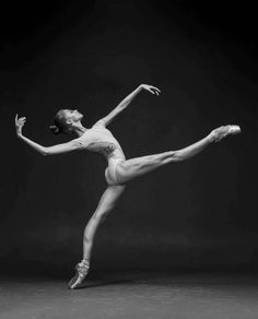 a woman in white leotard and ballet shoes is doing a split leg pose