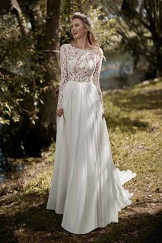 a woman standing in the woods wearing a wedding dress with long sleeves and sheer lace