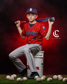 a young boy holding a baseball bat and sitting on top of a bucket with balls