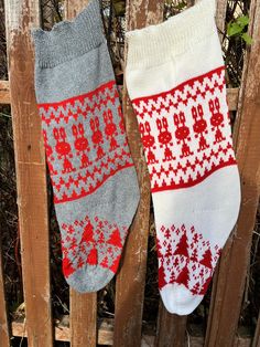 two knitted socks hanging on a wooden fence next to each other with red and white designs