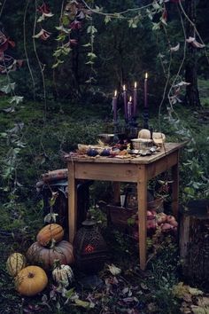 a table with candles and pumpkins on it in the middle of a forest filled with leaves