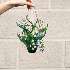 a hand holding a glass vase with flowers hanging from it's side on a chain