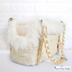 a white purse sitting on top of a table next to a brick wall with a gold chain around it