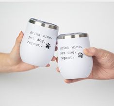 two white wine tumblers with words on them being held by someone's hand