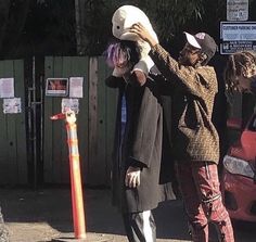 two people are standing on the street and one is holding a child's head