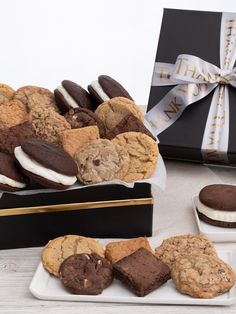 a box filled with cookies and chocolates on top of a white plate next to a black box