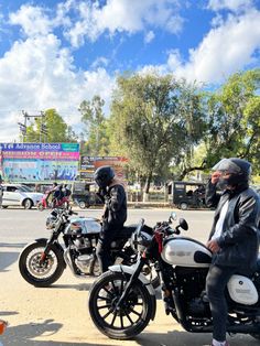 two men are sitting on their motorcycles in the middle of the street while another man stands next to them