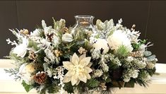 a vase filled with white flowers and greenery on top of a mantle next to a candle