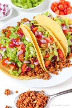 two tacos with lettuce, tomatoes and other toppings on a white plate