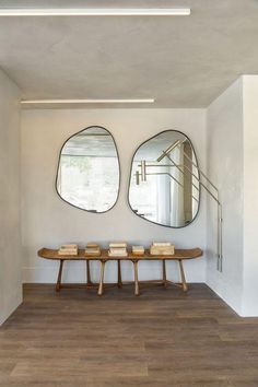 two circular mirrors hang on the wall above a bench in a room with wooden floors