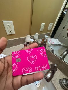 a person holding up a pink card in front of a bathroom sink with the word ama on it