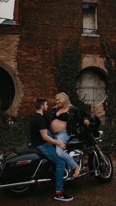 a pregnant woman sitting on the back of a motorcycle next to a man in jeans