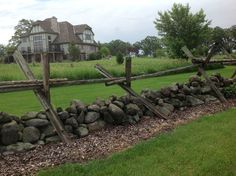 a wooden fence made out of rocks in front of a large house on a hill