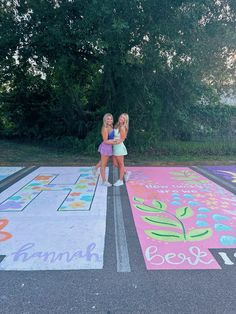 two girls are standing in the middle of a parking lot with chalk drawings on it