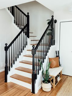 a white staircase with black railings and wooden steps next to a potted plant