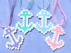 four different colored cross and anchor ornaments on a blue background with pink, purple, and white ribbons