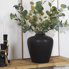 a black vase sitting on top of a wooden table next to a candle and some plants