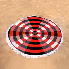 a red black and white round beach towel laying on the sand in the sand dunes