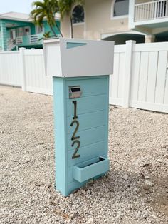 a blue mailbox sitting on top of gravel next to a white fence and palm trees