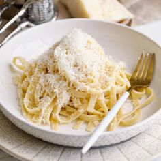 a white plate topped with pasta covered in parmesan cheese next to a fork