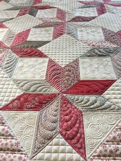 a close up of a quilt on a bed with red and white designs in the middle