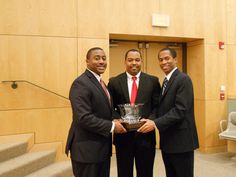 three men in suits standing next to each other with a trophy on their lapel