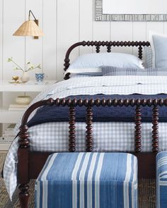 a bed with blue and white striped sheets, pillows and foot stools next to it